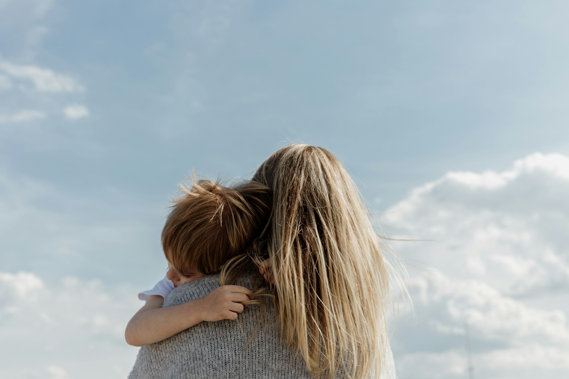 woman-holding-child-from-behind-against-cloudy-sky